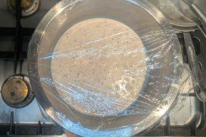 blood orange custard ice cream base in a stainless bowl covered with plastic wrap.