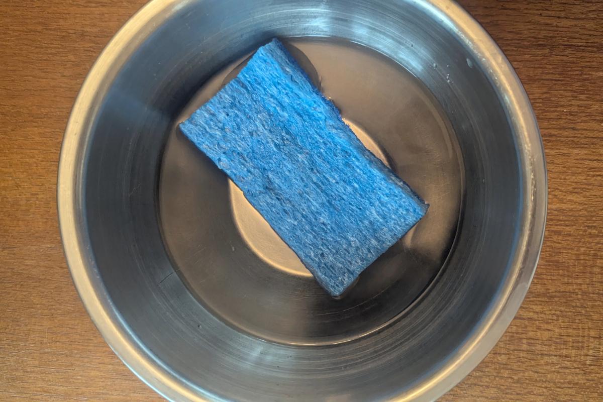 overhead view of a stainless steel bowl filled with water with a blue sponge floating inside.