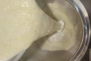 straining cooked custard into a bowl through a fine-mesh sieve.