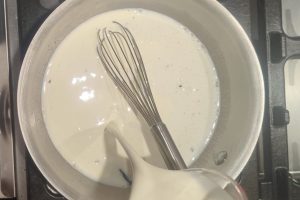 pouring heavy cream into a saucepan with milk, sugar, guar gum, and skim milk powder.