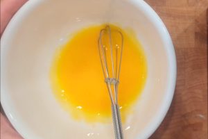 egg yolk in a bowl with a mini whisk.