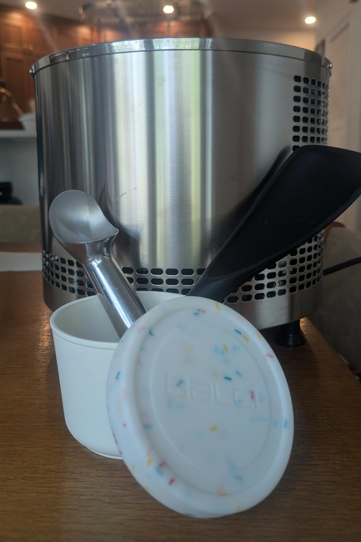 an ice cream scoop and ice cream spatula in a reusable ice cream pint container in front of a lello 4080 ice cream machine.