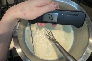 a thermometer reads 75°F dipped into ice cream base in a stainless bowl with a whisk.