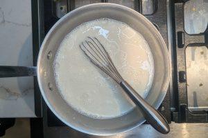 milk poured into dry ingredients in a saucepan with a whisk.