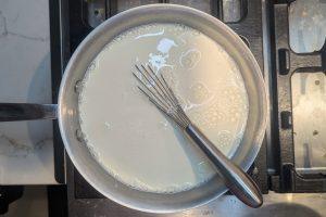 cream added to milk and dry ingredients for ice cream base in a saucepan with a whisk.