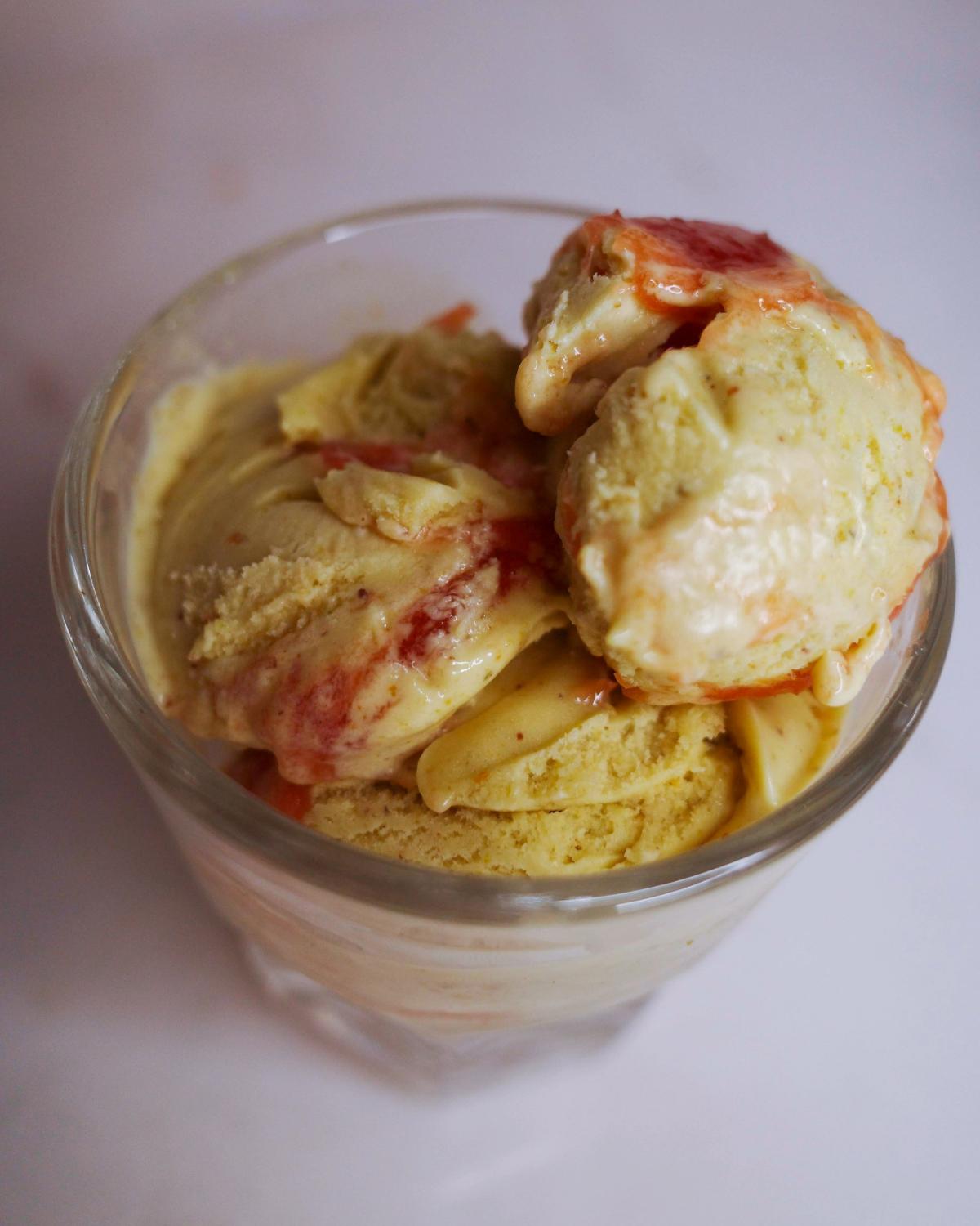 three-quarters view of three scoops of pistachio ice cream with rhubarb jam in a glass.