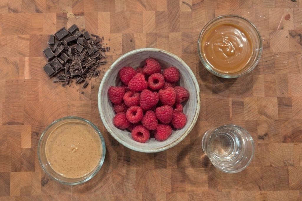 overhead view of chopped chocolate, nut butter, raspberries, caramel sauce, and clear alcohol in separate containers on a butcher block -- all of these will change your ice cream base ratio.