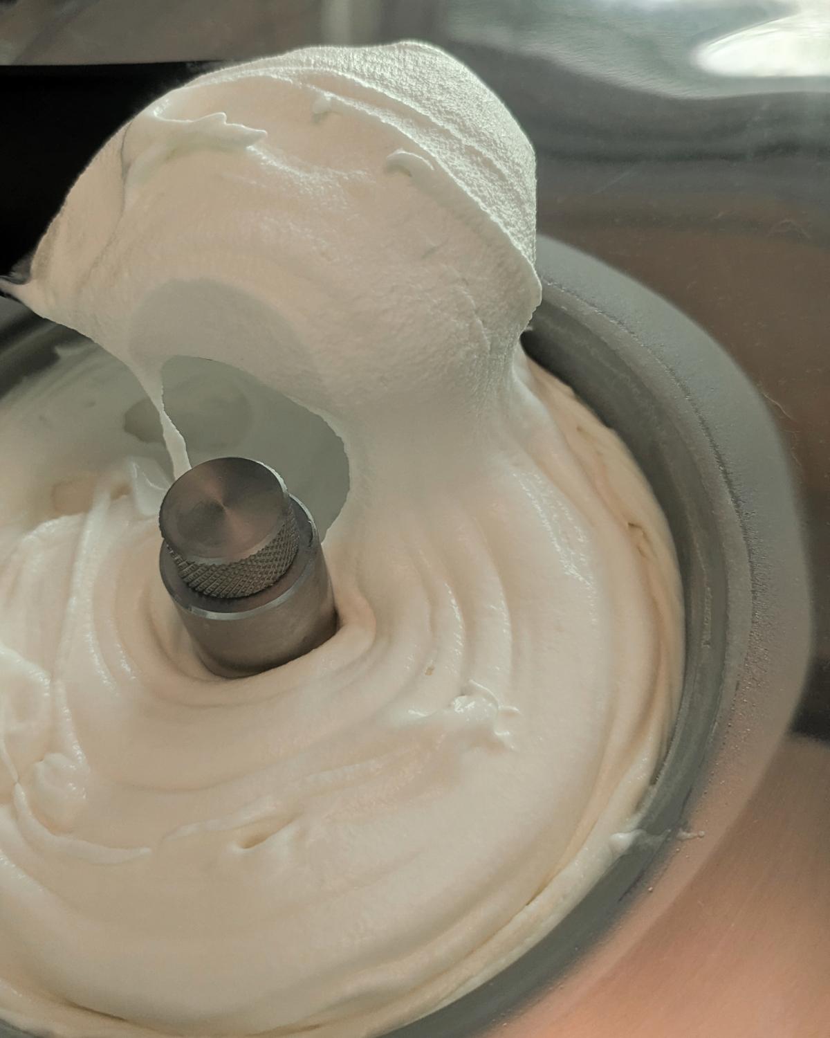 Lifting a scoop of freshly churned ice cream from the bowl of a compressor machine to show the correct soft-serve consistency when learning how long to churn ice cream.