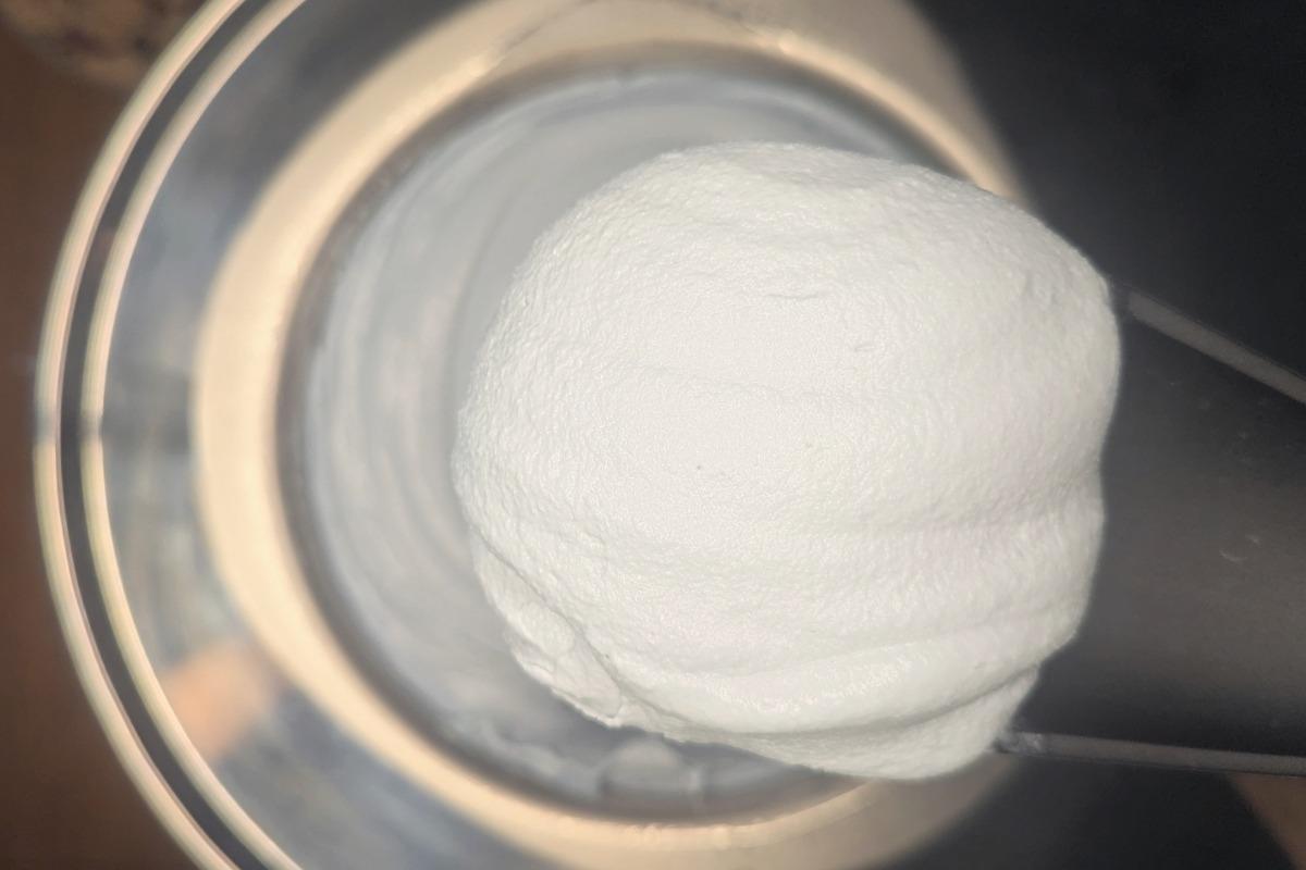pulling freshly churned blue vanilla ice cream from an ice cream maker bowl with a rubber spatula.