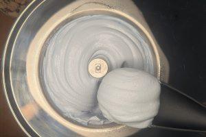 pulling freshly churned blue vanilla ice cream from an ice cream maker bowl with a rubber spatula.
