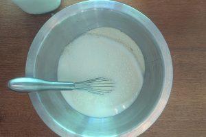 milk poured into a bowl of dry ingredients with a spoon.