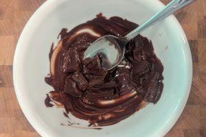 partially melted chocolate in a white bowl with a spoon.