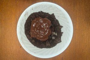 melted chocolate poured over crushed Oreo cookie crumbs in a bowl.