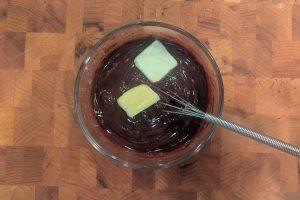 adding butter to chocolate ganache in a small bowl with a whisk.