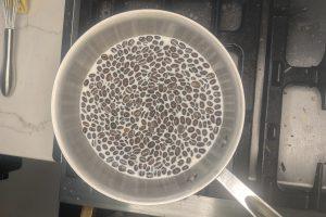 coffee beans added to steaming milk in a saucepan.