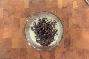chopped chocolate over warm cream in a glass bowl.