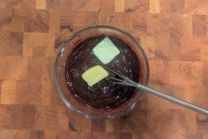 adding butter to chocolate ganache in a glass bowl.