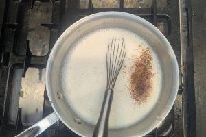 adding cinnamon and nutmeg to custard ice cream base in a saucepan with a whisk.
