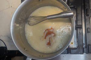 apple cider syrup added to caramel in a saucepan with a whisk.